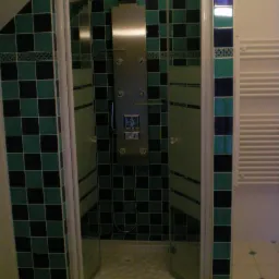 Kabina prysznicowa z hydromasażem, wyłożona kwadratowymi płytkami w kolorach zieleni i czerni, z elementami dekoracyjnymi w postaci pasków z ornamentami.