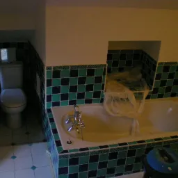 Łazienka w trakcie remontu: widoczna wanna zabezpieczona folią, nowa glazura w odcieniach zieleni i granatu, oraz toaleta w małej wnęce.