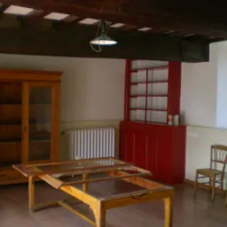 Pusta przestrzeń z drewnianą szafą z przeszklonymi drzwiami, czerwonym regałem, grzejnikiem i rozłożonym drewnianym stołem z szklanym blatem w trakcie renowacji, pod sufitem widoczne drewniane...