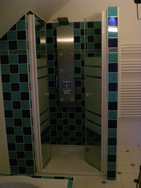 Kabina prysznicowa z hydromasażem, wyłożona kwadratowymi płytkami w kolorach zieleni i czerni, z elementami dekoracyjnymi w postaci pasków z ornamentami.