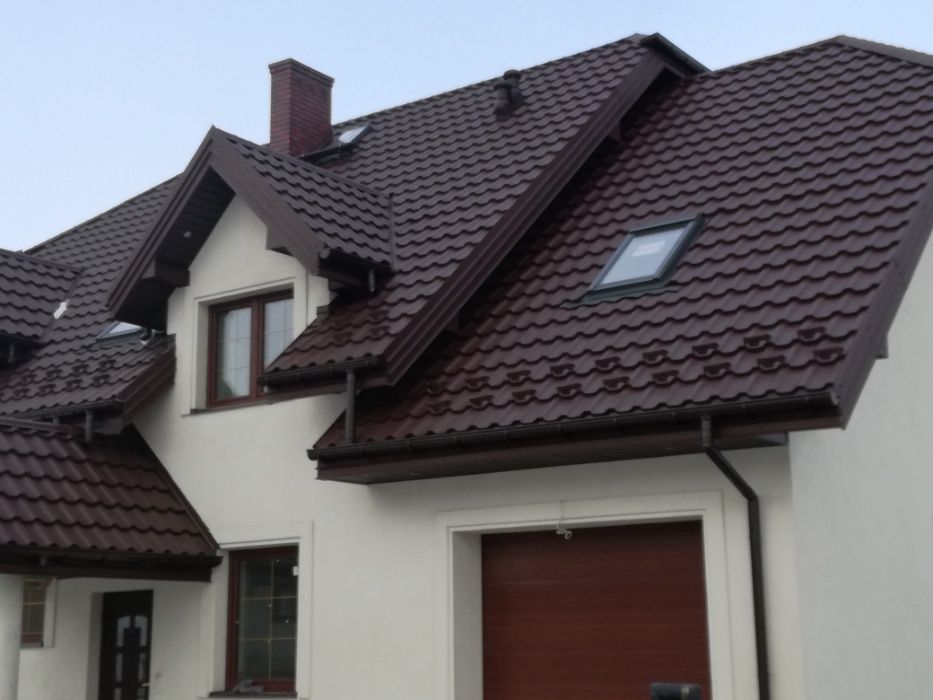 Dom z nowym, brązowym dachem z blachodachówki, widoczny komin, okno dachowe i rynny w tym samym kolorze, elewacja biała.