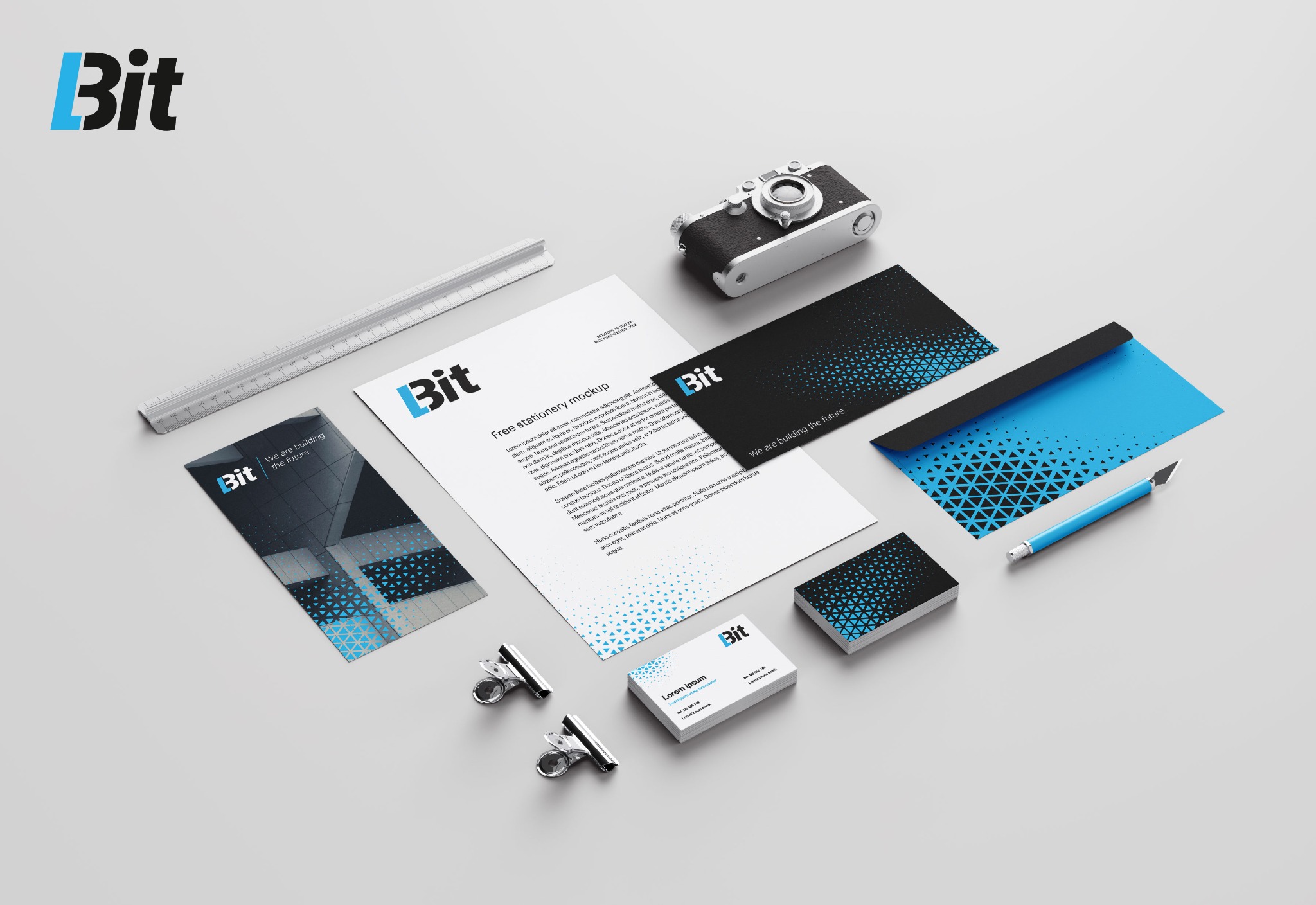 Zestaw materiałów biurowych z logo firmy 'Bit' na jasnoszarym tle, zawierający wizytówki, papier firmowy, kopertę, notes, długopis, linijkę, spinacze biurowe i aparat retro.