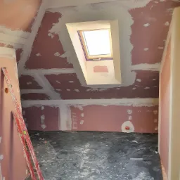 Poddasze w trakcie remontu: płyty karton-gips na skosach i ścianach, spoiny zaszpachlowane, okno dachowe w zabudowie, czerwona drabina oparta o ścianę, podłoga zabezpieczona folią.