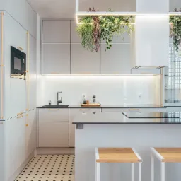 Nowoczesna, jasna kuchnia w Gdańsku z wyspą i dekoracyjnymi roślinami zwisającymi z sufitu, oświetlona punktowo, z czarno-białą mozaiką na podłodze.
