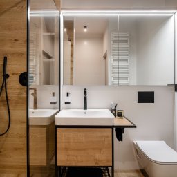Monika Wierzba-Krygiel Architektura i Wnętrza - Nowoczesna łazienka z drewnianymi akcentami, kwadratową umywalką nablatową, czarną armaturą, toaletą podwieszaną i ścianą z motywem roślinnym.