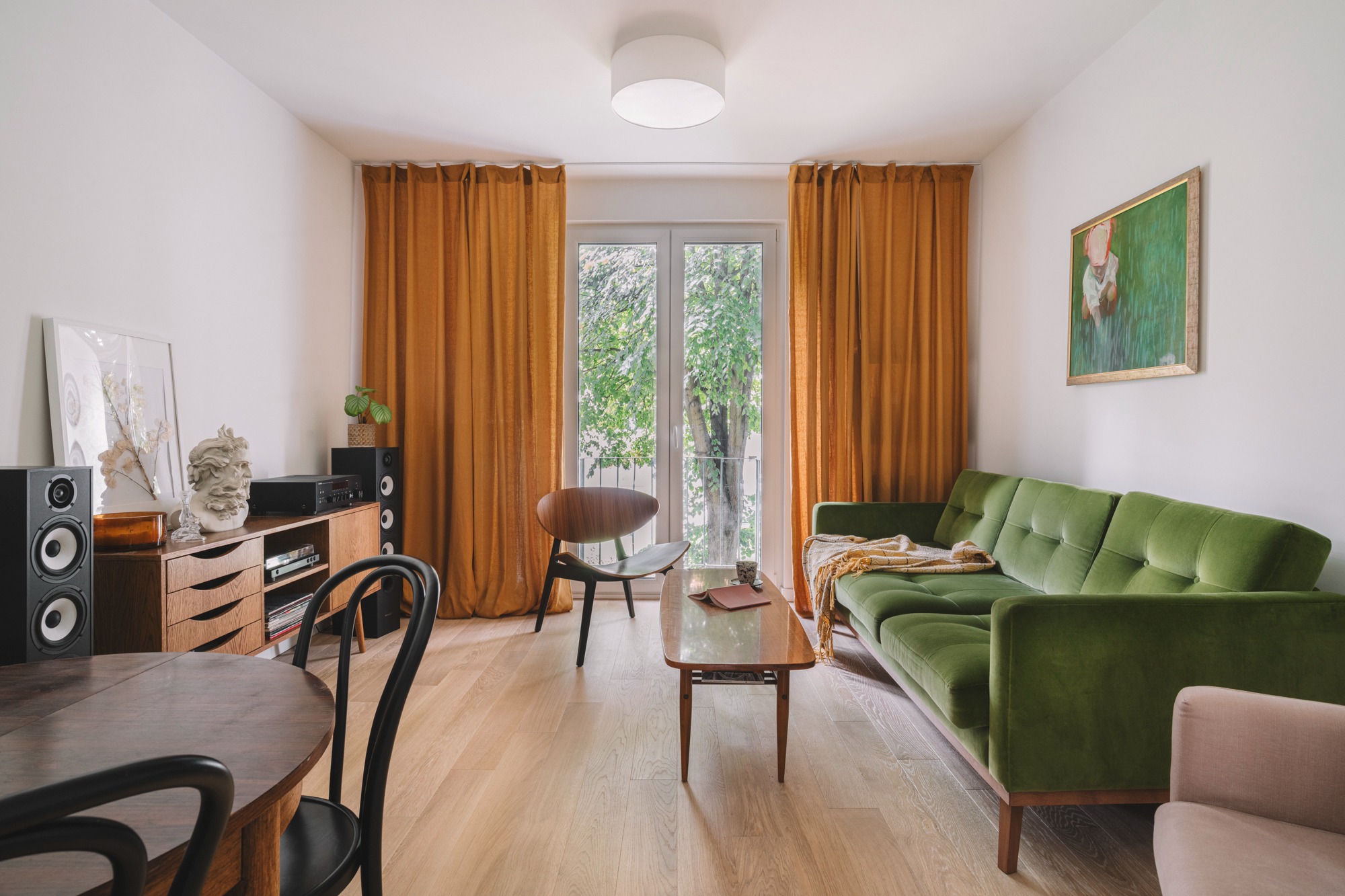 Salon w stylu retro z zieloną sofą, drewnianym stolikiem kawowym, gramofonem i kolumnami głośnikowymi, oświetlony naturalnym światłem wpadającym przez okno z pomarańczowymi zasłonami.
