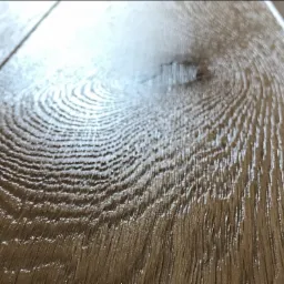 Błyszcząca, lakierowana podłoga z paneli drewnopodobnych, widoczne wyraźne usłojenie i subtelne refleksy światła.