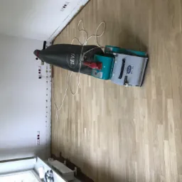 Profesjonalna szlifierka do parkietu marki Deva na częściowo wyszlifowanej drewnianej podłodze w jasnym odcieniu, widoczne ślady po listwach przypodłogowych.