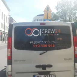 Tył srebrnego busa Renault Trafic z naklejką firmy Crew24 oferującej przewóz osób 24h, widoczny numer telefonu i logo firmy.