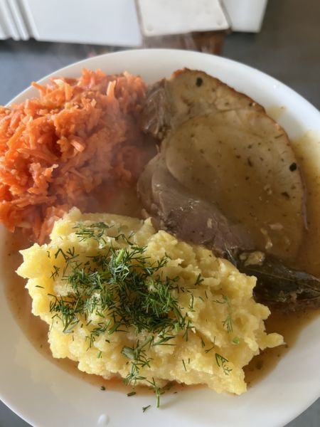 Apetyczny talerz z obiadem: pieczeń w sosie, puree ziemniaczane posypane koperkiem i surówka z marchewki. Para unosi się znad ciepłego dania.