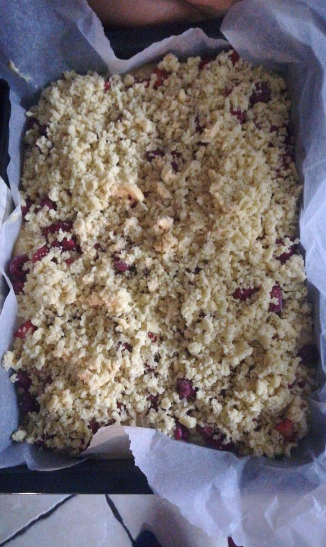 Kruchy placek z owocami w formie do pieczenia wyłożonej papierem, posypany kruszonką.