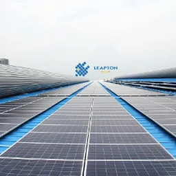 Rozległa instalacja fotowoltaiczna na dachu z blachy trapezowej pomalowanej na niebiesko, widok z góry, logo firmy Leapton Solar w tle.