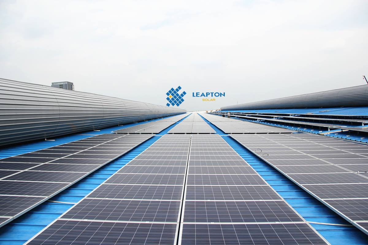 Rozległa instalacja fotowoltaiczna na dachu z blachy trapezowej pomalowanej na niebiesko, widok z góry, logo firmy Leapton Solar w tle.