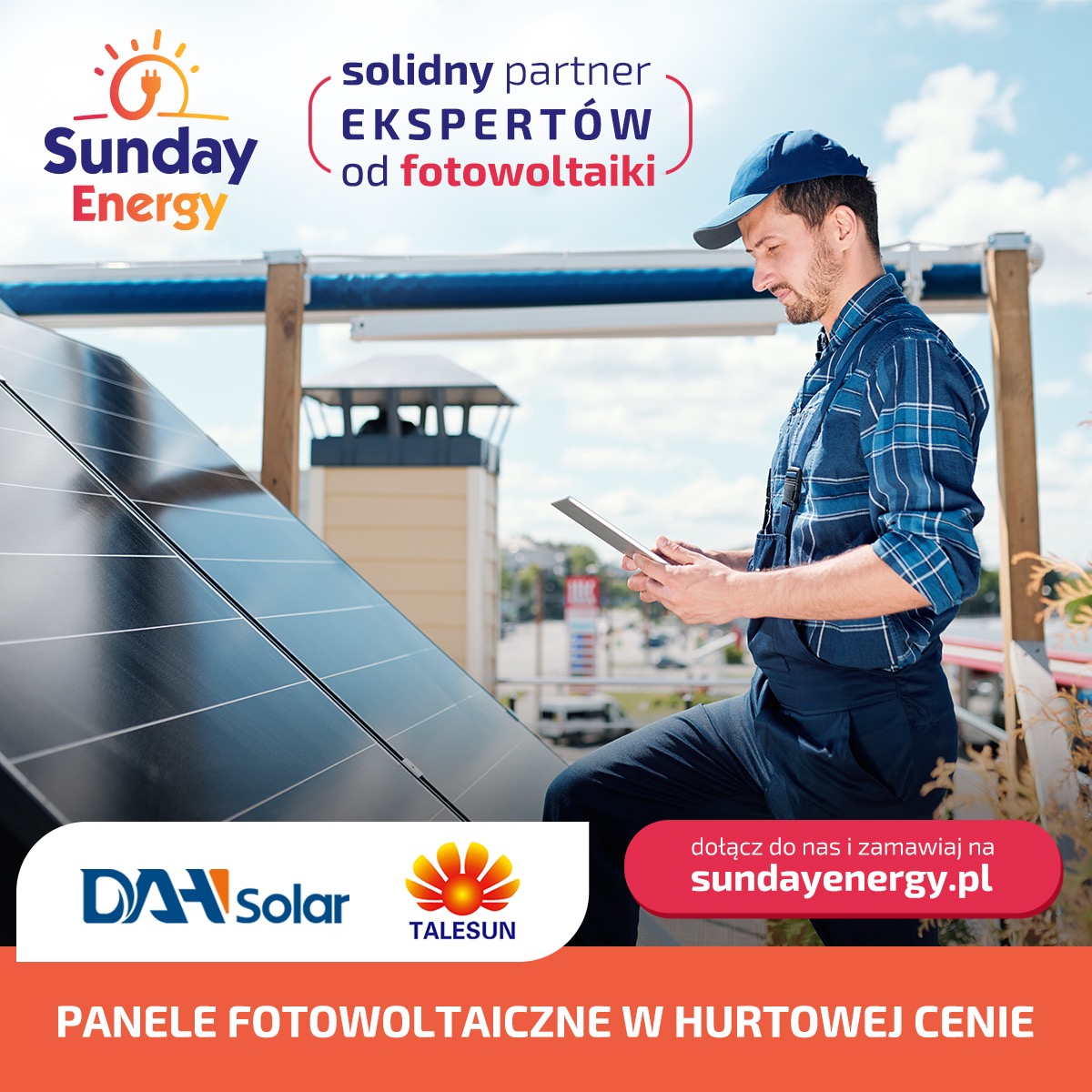 Instalator w niebieskim kombinezonie sprawdza dane na tablecie obok paneli słonecznych na dachu, w tle widoczny komin wentylacyjny.