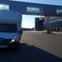 Biały Renault Master z wysoką zabudową, zaparkowany na tle nowoczesnego magazynu z rampami załadunkowymi i łącznikiem dla pieszych, widoczne tablice rejestracyjne LU 250GJ.