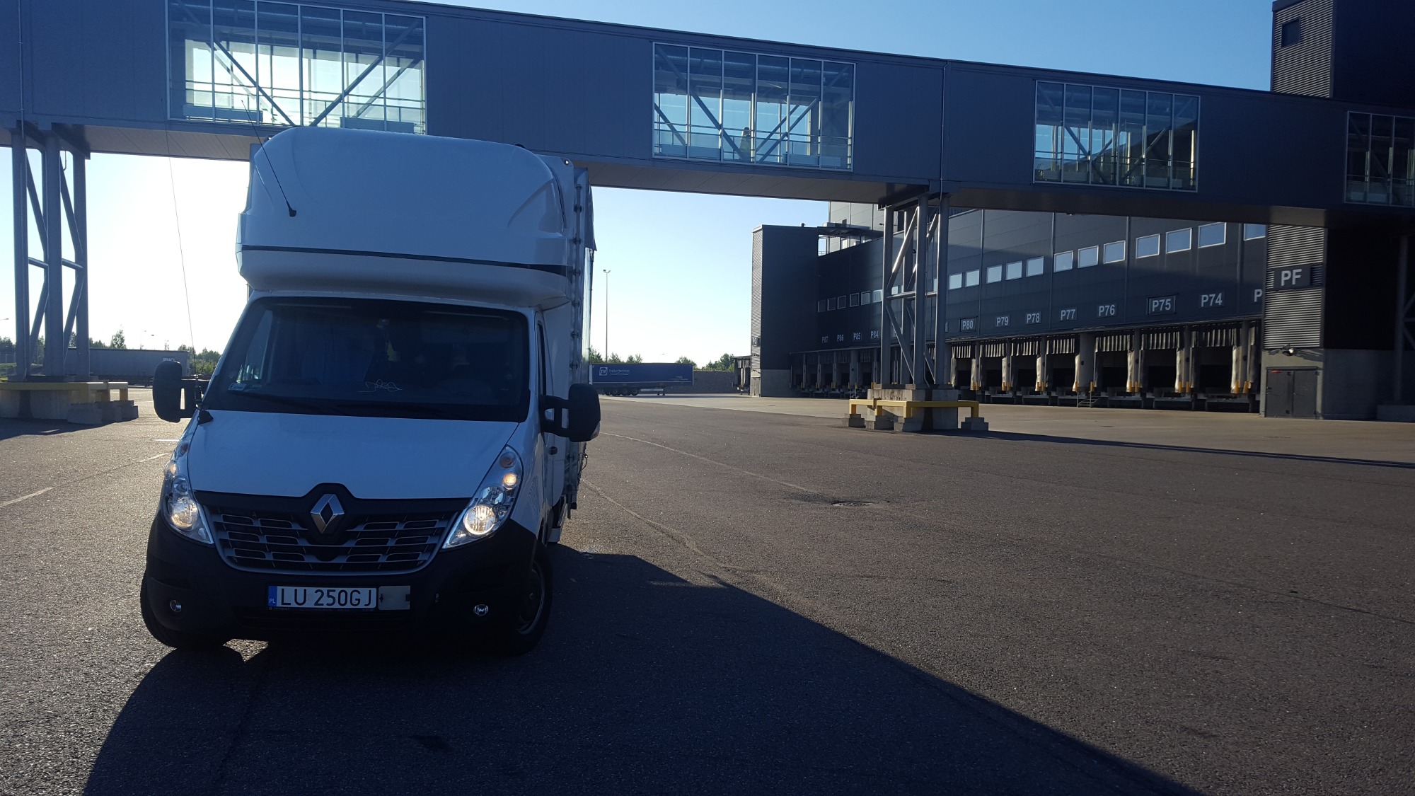 Biały Renault Master z wysoką zabudową, zaparkowany na tle nowoczesnego magazynu z rampami załadunkowymi i łącznikiem dla pieszych, widoczne tablice rejestracyjne LU 250GJ.