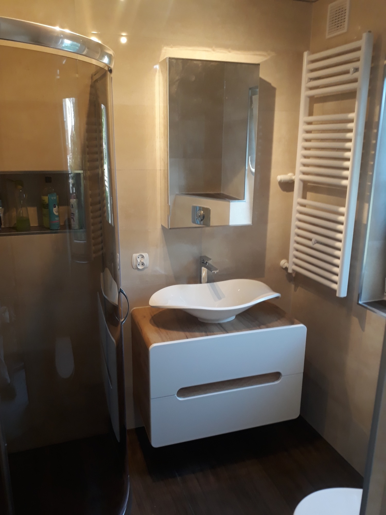 Nowoczesna łazienka z kabiną prysznicową, umywalką nablatową na szafce z drewnianym blatem i grzejnikiem drabinkowym.