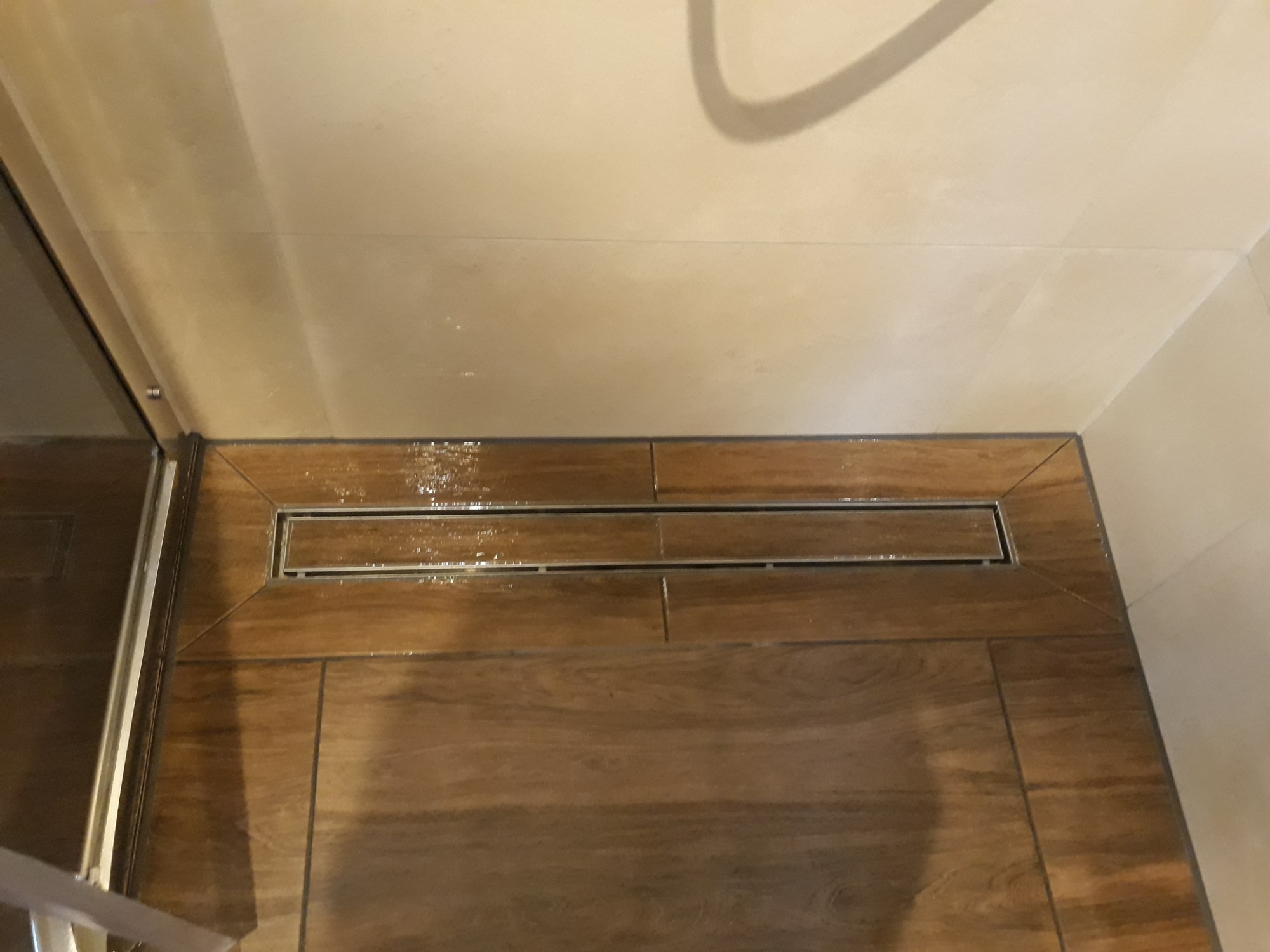 Ułożone płytki podłogowe imitujące drewno z odpływem liniowym w kabinie prysznicowej, widoczne ślady po uszczelnianiu fug.