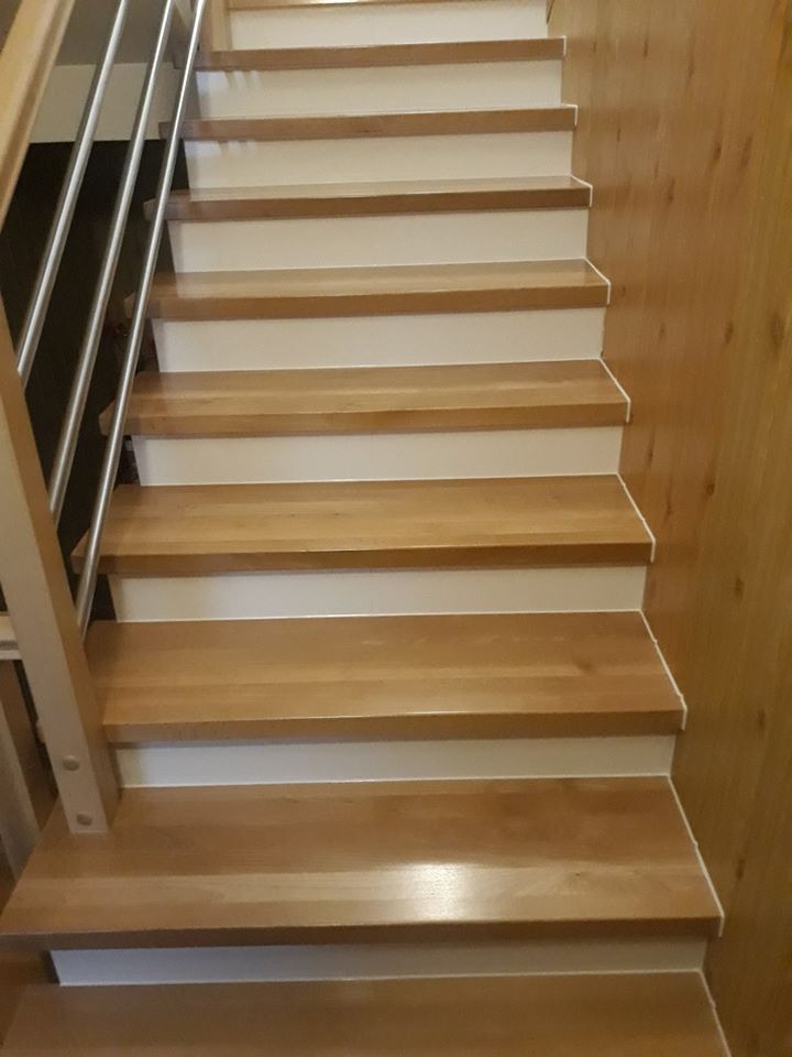 Drewniane schody z białymi podstopnicami i metalową balustradą, widok z dołu na górę, przy prawej ścianie boazeria z jasnego drewna.