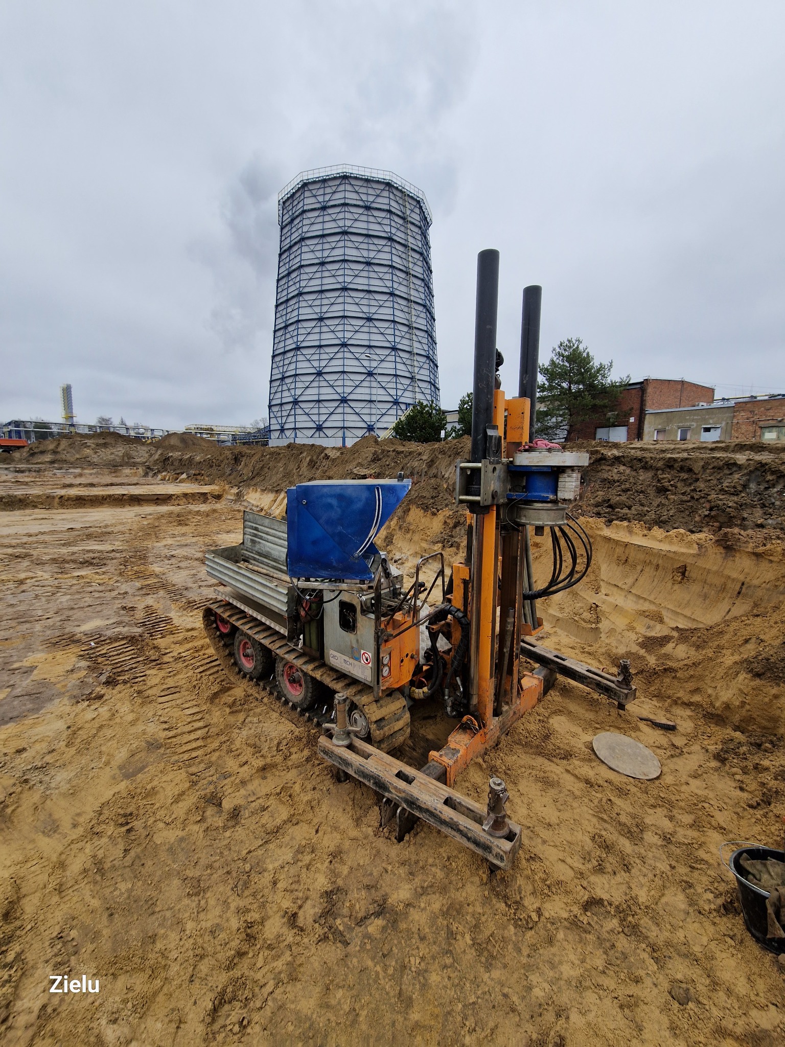 Wiertnica na gąsienicach podczas prac ziemnych we Wrocławiu, w tle widoczna chłodnia kominowa i wykop.