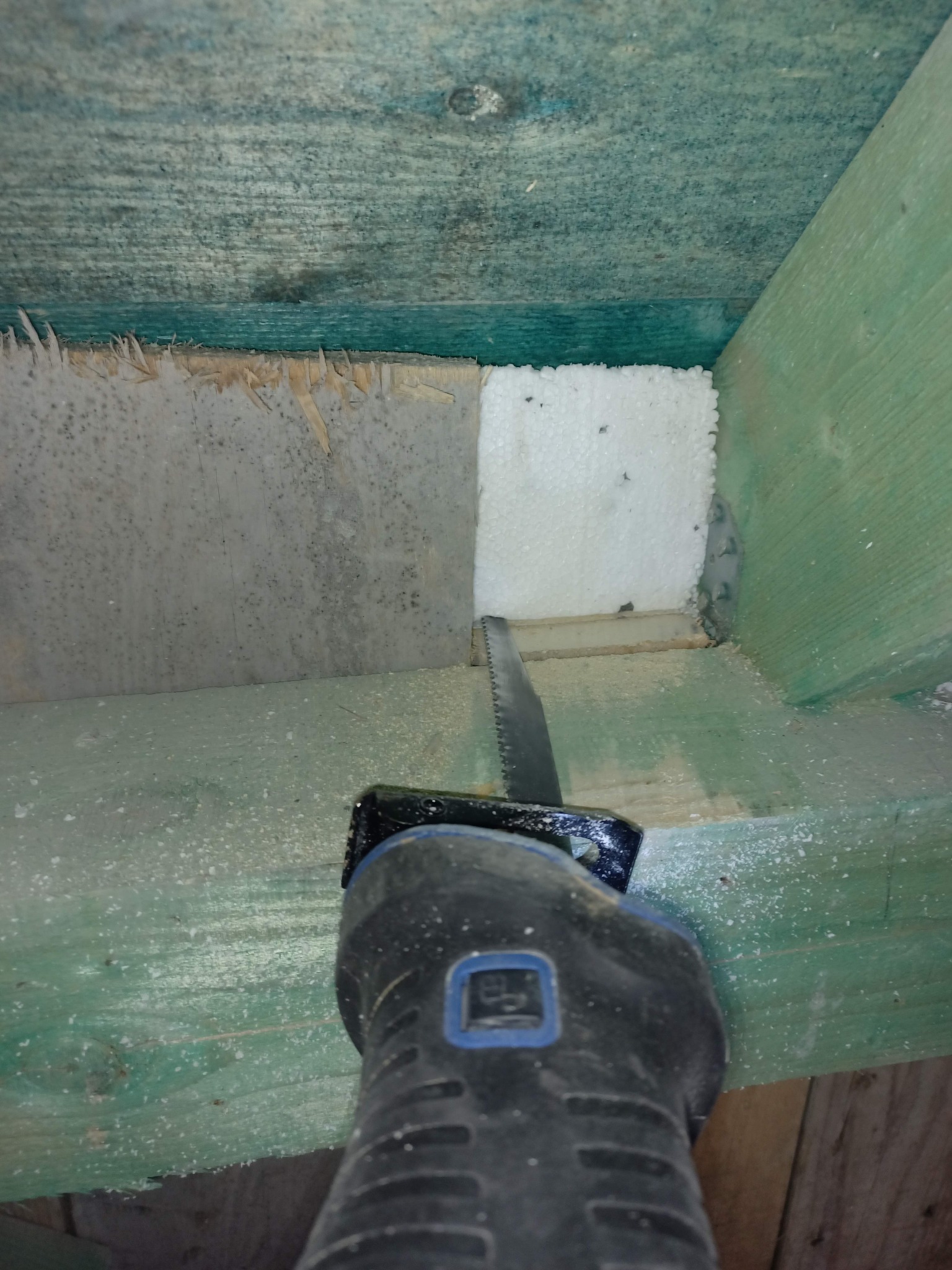 Docinanie białego styropianu piłą elektryczną w przestrzeni między drewnianymi elementami konstrukcyjnymi. Fragment ocieplenia w trakcie montażu.