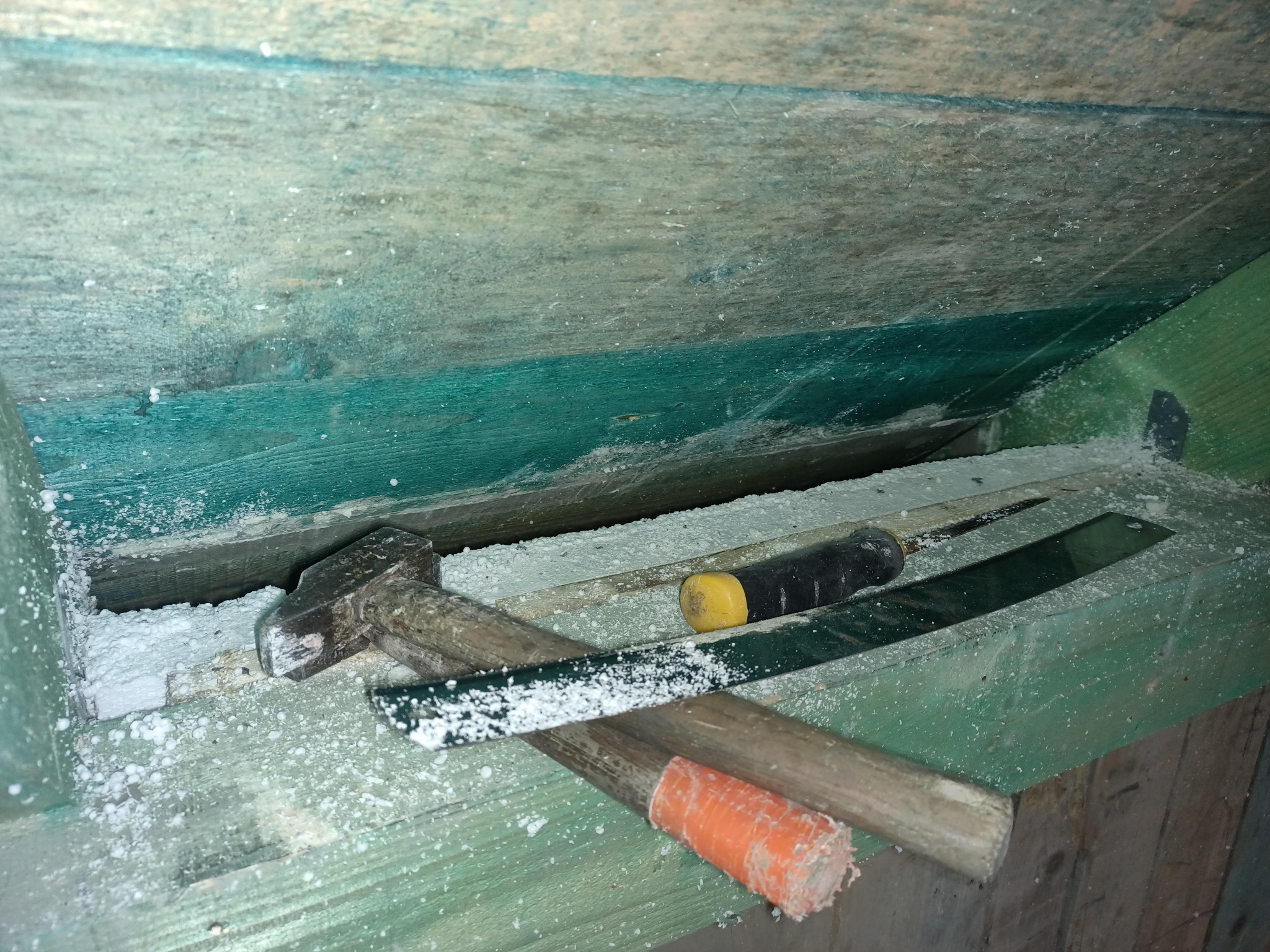 Drewniana konstrukcja pokryta białym granulatem, widoczny młotek i inne narzędzia, prawdopodobnie w trakcie prac związanych z izolacją poddasza.