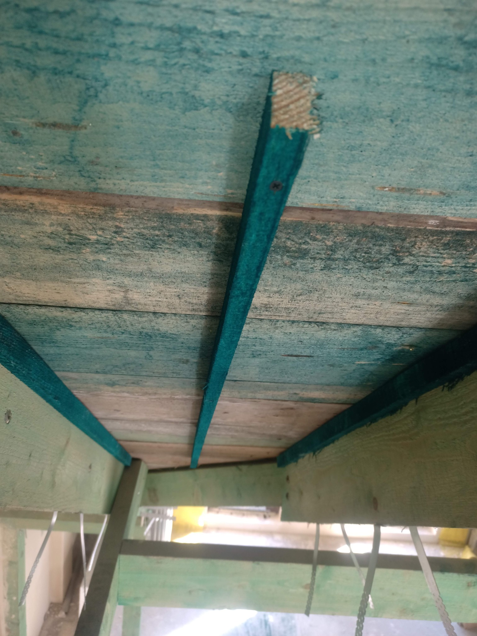 Drewniana konstrukcja dachu z elementami pomalowanymi na zielono, widok z dołu, z widocznymi listwami i elementami mocującymi.