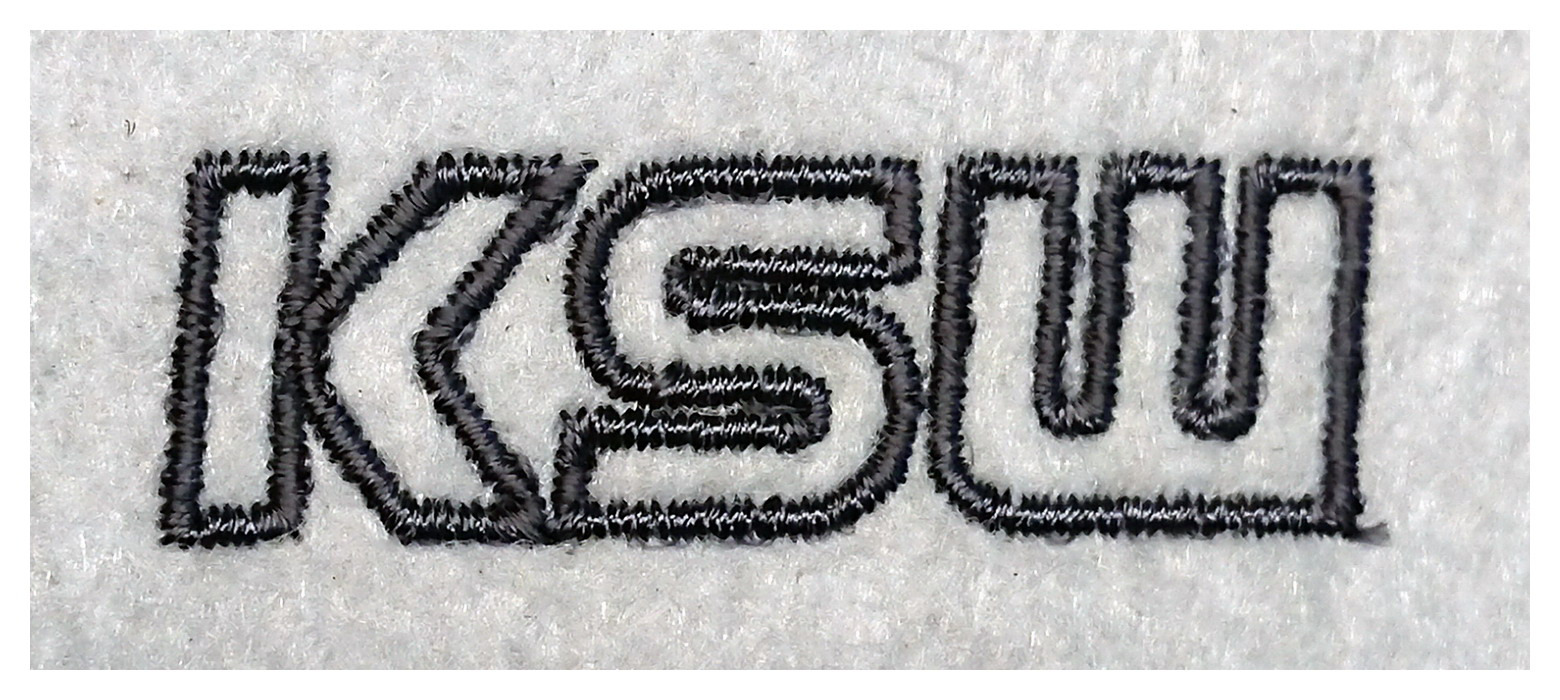 Haftowane czarną nicią logo 'KSW' na białym, filcowym materiale, widoczne z bliska detale ściegów.