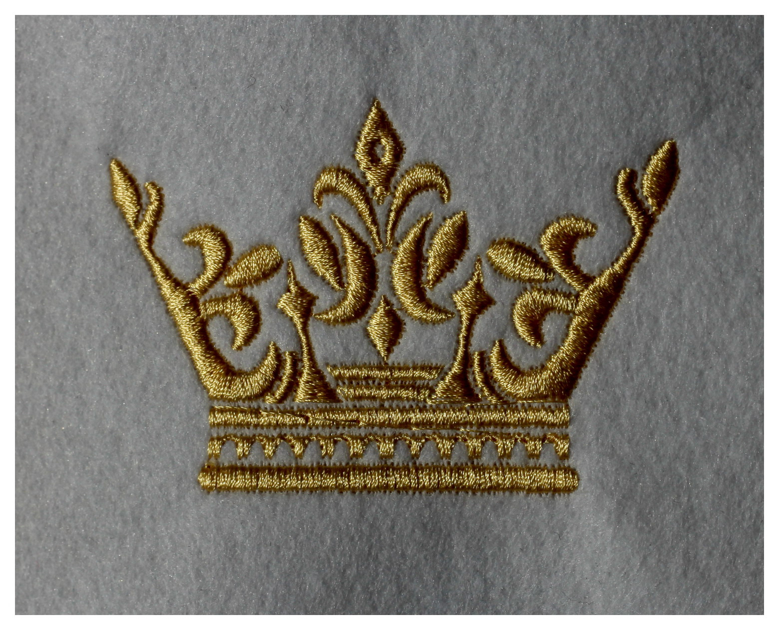 Złota korona wykonana techniką haftu na szarym, filcowym materiale.