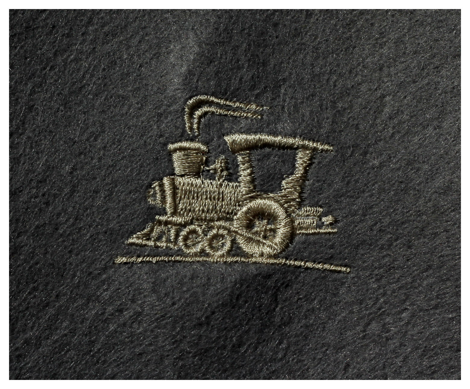 Szczegółowe zbliżenie na haftowaną lokomotywę w kolorze złamanej bieli na ciemnoszarym, filcowym materiale.