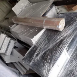 Meble zabezpieczone folią stretch w przestrzeni ładunkowej busa podczas przeprowadzki, widoczne elementy szafek, materac i drewniane listwy.