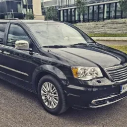 Czarny minivan Chrysler Town & Country zaparkowany na ulicy z nowoczesnym budynkiem biurowym w tle.
