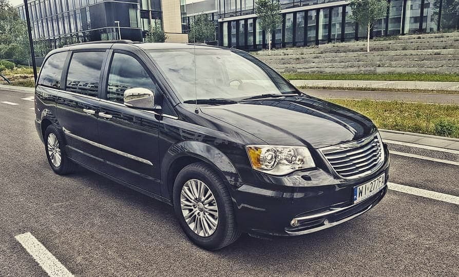 Czarny minivan Chrysler Town & Country zaparkowany na ulicy z nowoczesnym budynkiem biurowym w tle.