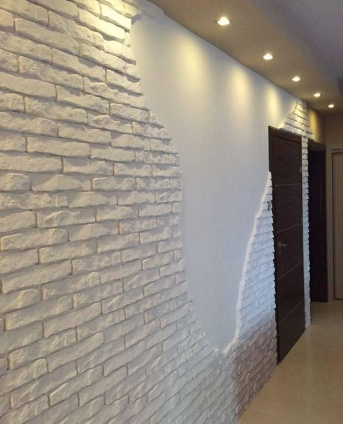 Wykończenie wnętrza z częściowo ułożoną dekoracyjną białą cegłą na ścianie, widoczne halogenowe oświetlenie sufitowe i fragmenty drzwi.