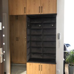 FIN-DREW CIĘŻCY KLAUDIA CIĘŻKA - Zabudowa przedpokoju z szafą, siedziskiem z tapicerowanym panelem ściennym i lustrem, wykończona w drewnie o jasnym odcieniu, z czarnymi uchwytami.