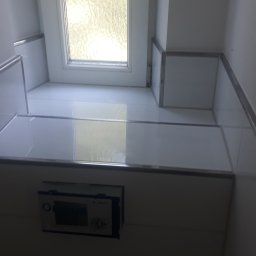 Tomasz - Biała, wykafelkowana półka pod oknem w łazience z zamontowanym sterownikiem do spłuczki, widok od dołu.