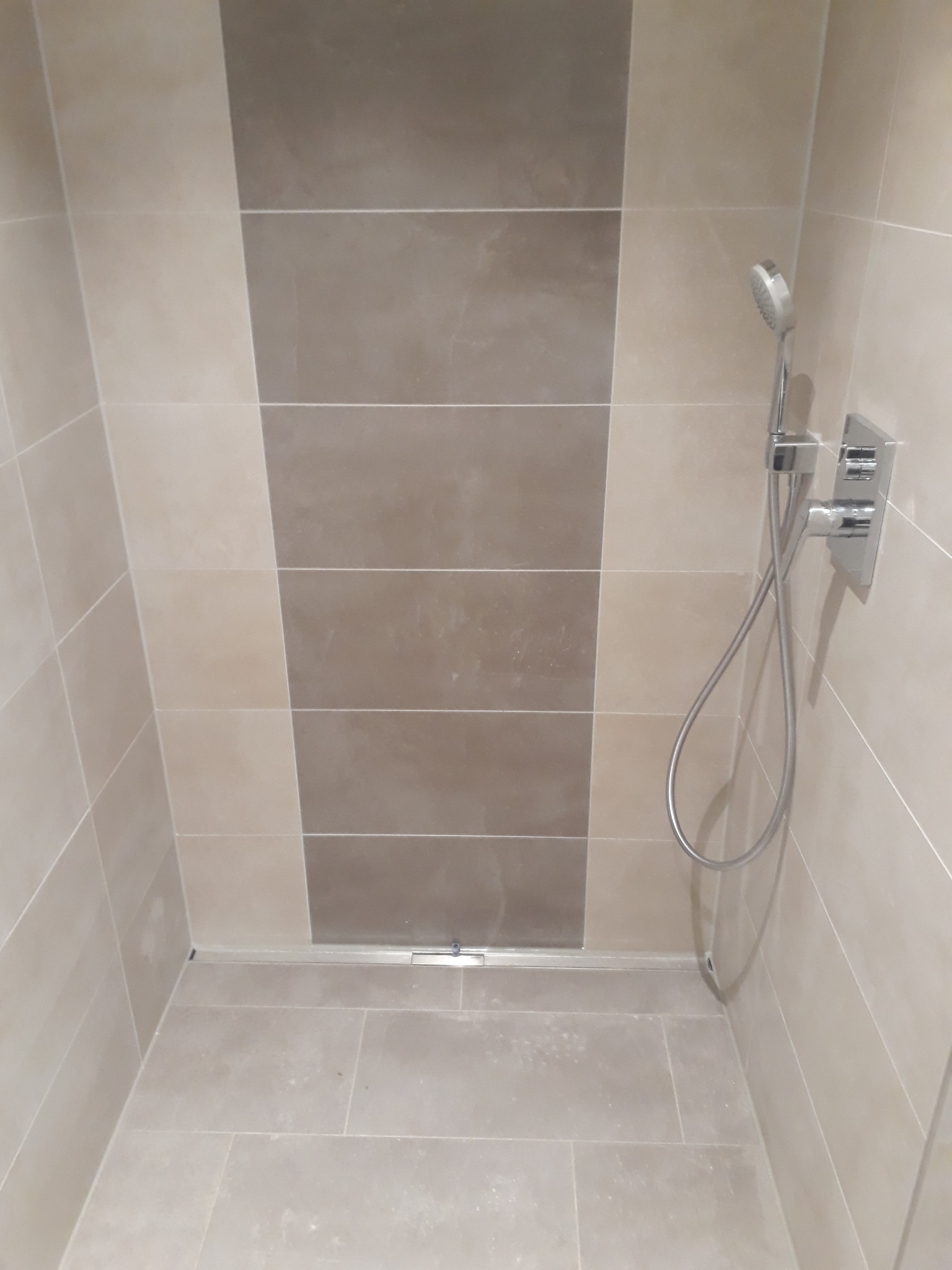 Nowoczesny prysznic z beżowymi i brązowymi płytkami, deszczownicą i odpływem liniowym w podłodze.