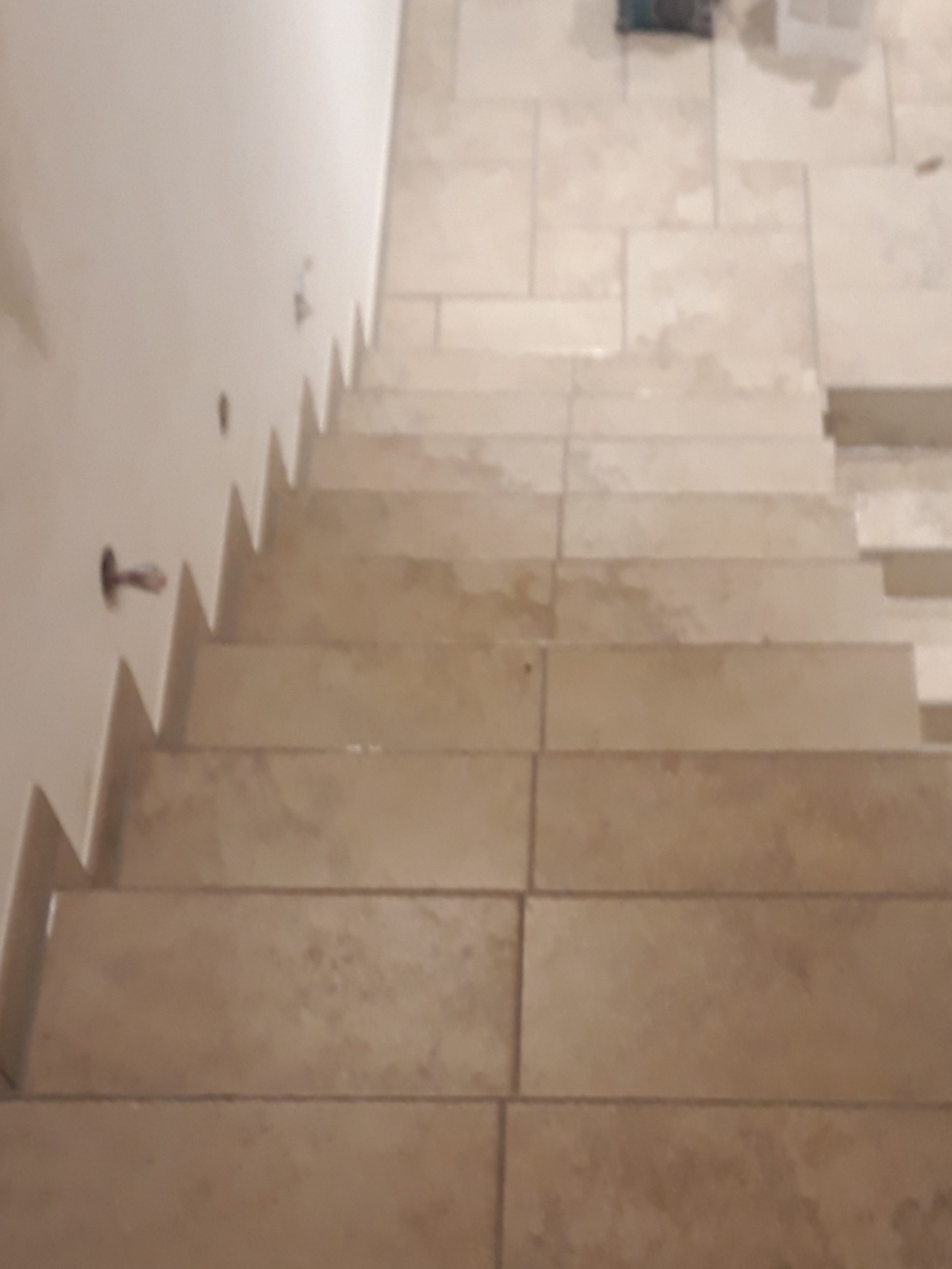 Wykończone schody wewnętrzne z beżowych płytek ceramicznych, widok z góry, z widocznymi punktami oświetleniowymi w ścianie.