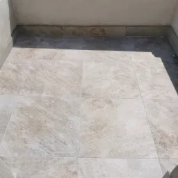 Jasne, kwadratowe płytki podłogowe z delikatnym wzorem kamienia, wyłożone na balkonie z niską, pomalowaną na biało ścianką, widok z góry.