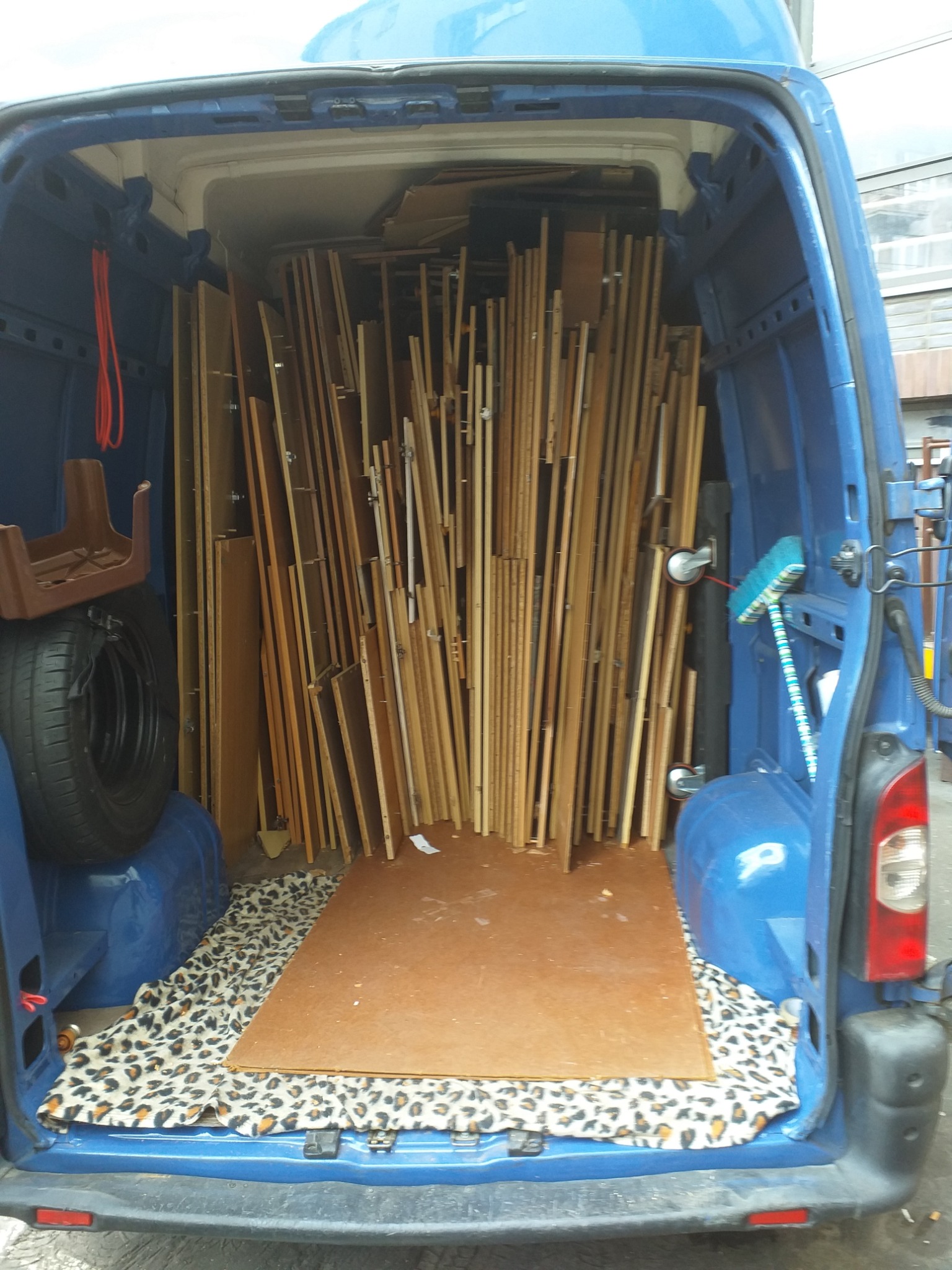 Wnętrze niebieskiego busa wypełnione po brzegi płytami drewnianymi różnej wielkości, dodatkowo koło zapasowe, szczotka i dywanik w panterkę.