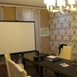 Sala konferencyjna z projektorem i ekranem, przygotowana do szkolenia, z dekoracyjną tapetą w tle i eleganckim żyrandolem.