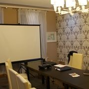 Sala konferencyjna z projektorem i ekranem, przygotowana do szkolenia, z dekoracyjną tapetą w tle i eleganckim żyrandolem.