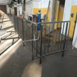 Metalowa balustrada ochronna w hali produkcyjnej, spawana konstrukcja z profili stalowych, w tle butla z gazem technicznym i otwarte drzwi.