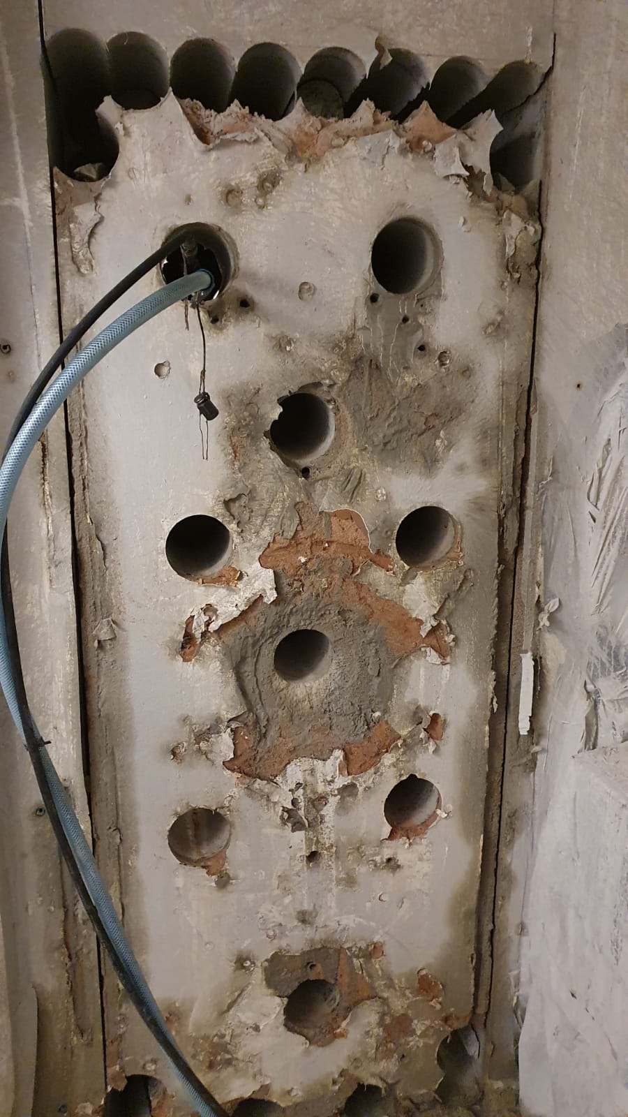 Ściana po wierceniu otworów, widoczne ślady po rdzeniu wiertniczym, fragment węża doprowadzającego wodę do wiertła.