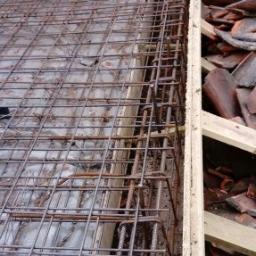 Phu.Jon-Bud Joanna Jagielska - Siatka zbrojeniowa ułożona na deskowaniu, widok z góry, fragment muru z cegły w tle.