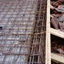 Siatka zbrojeniowa ułożona na deskowaniu, widok z góry, fragment muru z cegły w tle.