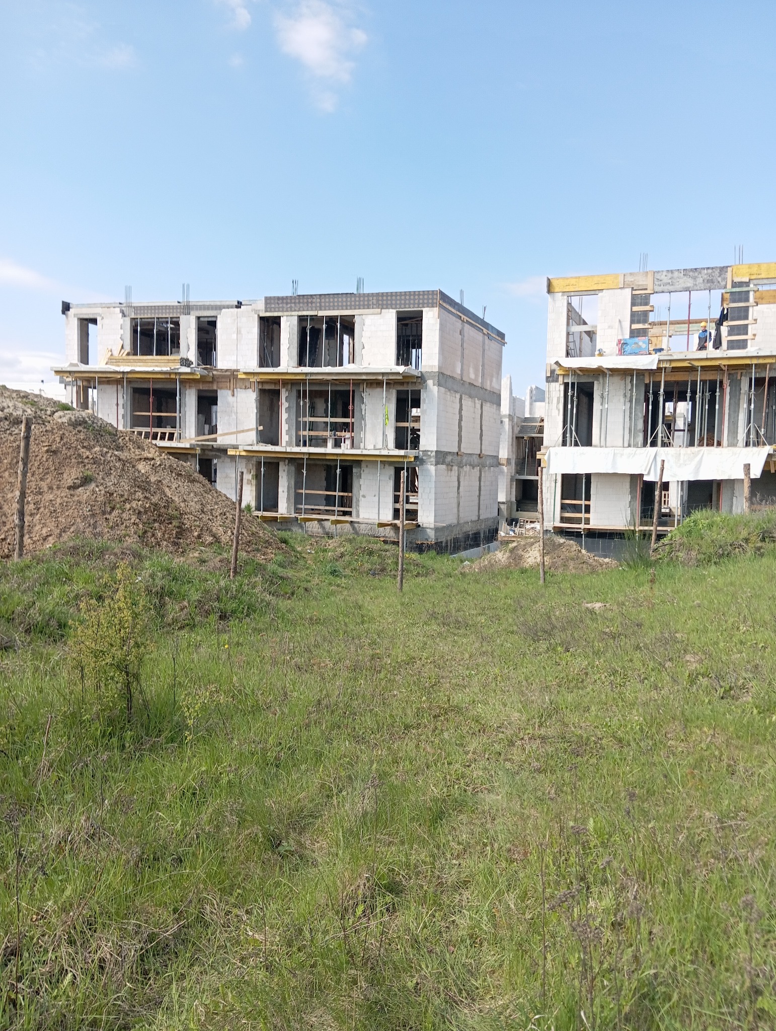 Budowa wielorodzinnego budynku z betonu komórkowego w stanie surowym otwartym, widoczne szalunki, zbrojenia i stos budowlany ziemi na pierwszym planie.