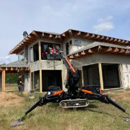 Montaż okna w surowym budynku jednorodzinnym z użyciem specjalistycznego dźwigu; widoczny pracownik w czarnej koszulce i spodniach.