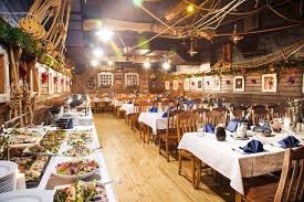 Uroczysta sala restauracyjna z nakrytymi stołami i bufetem pełnym potraw, dekoracje świąteczne na ścianach, rustykalny wystrój z elementami marynistycznymi.