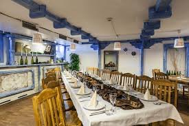 Uroczysty stół bankietowy z białym obrusem, nakryty dla wielu gości, z drewnianymi krzesłami i dekoracyjnymi elementami w kolorze niebieskim na suficie i ścianach.